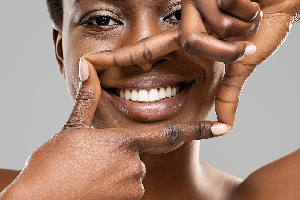 Frame your smile. Beautiful african woman framing her perfect white teeth with fingers, closeup