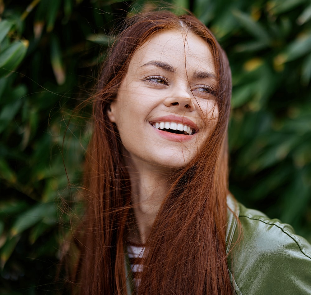 Portrait of happiness woman with red flying hair smile with teeth walking in the city in the park against a backdrop of green bamboo leaves, spring in the city