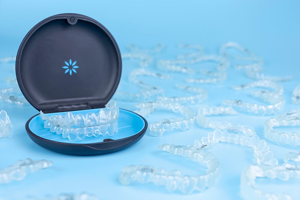 Invisible retainers case with orthodontic aligner brackets thrown around. Black plastic dental container for invisalign braces on blue background