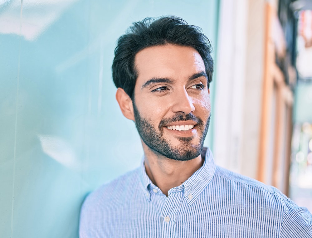 Young hispanic man smiling happy leaning on the wall at the city.